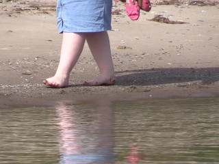 On high heels and bare feet on the sand, plumplegs walk along the_shore.