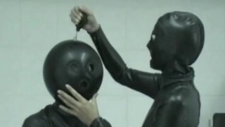 Two Girls Dressed In Black Latex Catsuits With Ballhoods And Inflated Mittens