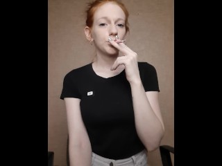 Redhead girl smokes a cigarette,hair is gathered in a_bun